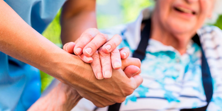 Carer holds their smiling, elderly clients hands.